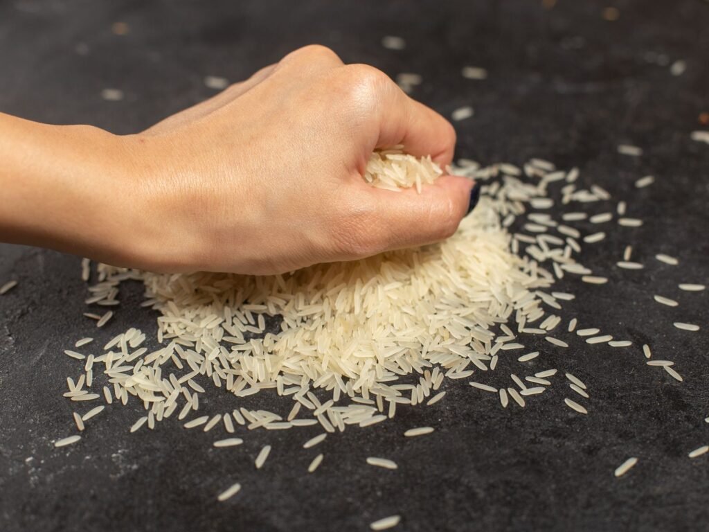 A hand checking a sample of long grain rice on a dark table